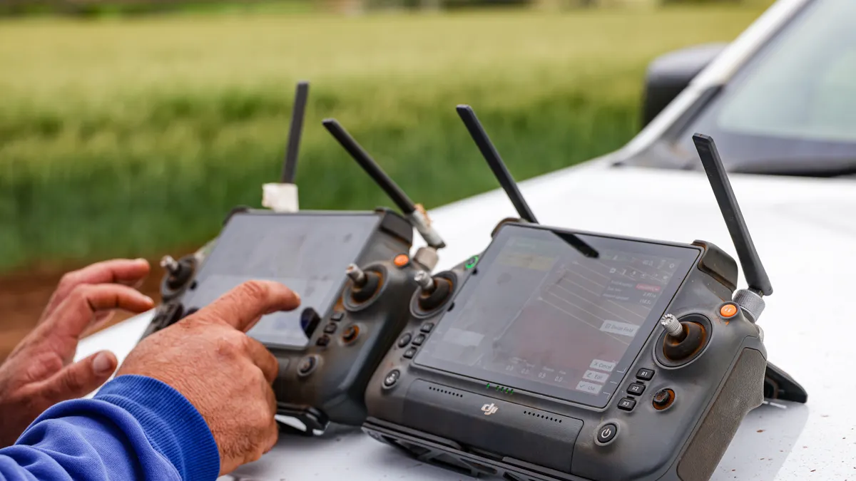 Hands operating remote-control consoles beside a farm vehicle